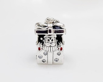 May include: A silver charm in the shape of a gift box with a Santa Claus design. The charm features a bow on top, a Santa face, red accents, and clear crystal embellishments. A festive holiday-themed accessory.