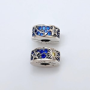 May include: Two silver charm bracelets with blue and yellow gemstones. The charms feature a crescent moon, stars, and a sun.