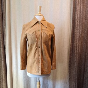 May include: A brown suede leather jacket with a collared button-up front and two flap pockets.