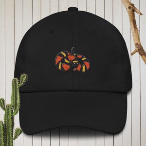 Puede incluir: Gorra de béisbol negra con una imagen bordada de una serpiente roja, naranja y amarilla.