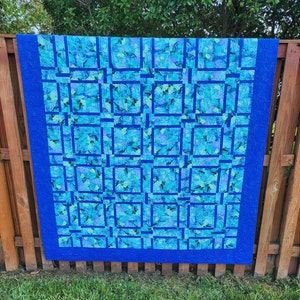 May include: A blue and green patchwork quilt with a geometric pattern. The quilt is made of squares and rectangles, and the fabric is a mix of blue and green shades.