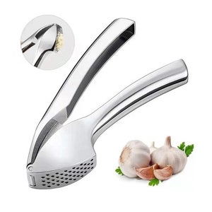 Peut inclure: Un presse-ail en argent avec une surface texturée et une poignée. Le presse-ail est conçu pour écraser les gousses d'ail et est présenté avec des gousses d'ail entières.
