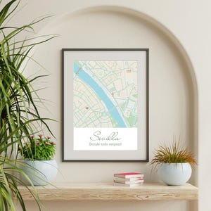 Può includere: Una stampa incorniciata con una mappa di Siviglia, Spagna, che mostra una rete stradale dai toni chiari, un fiume blu e una piccola icona a forma di cuore rosso. Sotto la mappa, il testo riporta Sevilla e Donde todo empezó in grigio scuro.