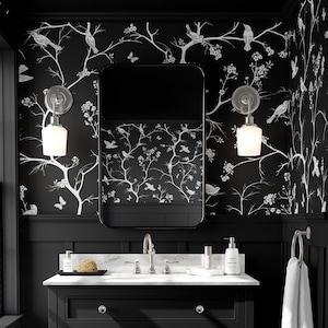 May include: A black and white bathroom vanity with a white marble countertop and a black cabinet with three drawers. The vanity has a mirror above it with a black frame and two wall sconces with white glass shades. The walls are covered in black wallpaper with a white floral pattern.