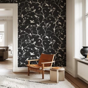 May include: A black and white wallpaper with a repeating pattern of branches and birds. The wallpaper is in a living room with a chair and a side table.
