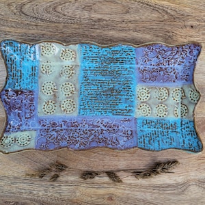 May include: A ceramic serving tray with a wavy edge and a patchwork design. The tray is decorated with a blue, purple, and white floral pattern.