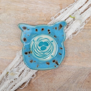 May include: A blue ceramic dish with a white nest and turquoise eggs design. The dish has a speckled glaze and a unique shape.