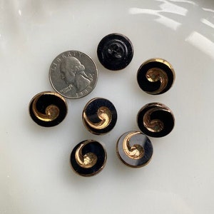 May include: Eight black and gold swirl buttons. The buttons have a black background with a gold swirl design.