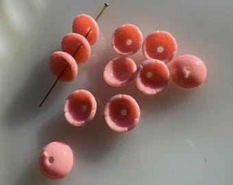 May include: A collection of pink beads with a central hole, some strung on a pin. The beads have a flower-like shape with a slightly darker pink hue in the center. Ideal for jewelry making.