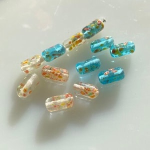 May include: Assortment of colourful glass beads with floral patterns. The beads are in shades of blue, white, and orange.