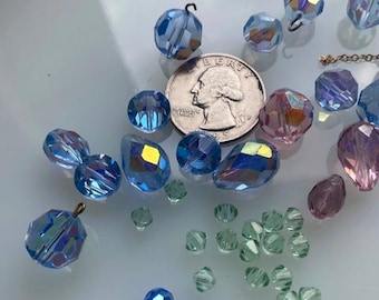 Könnte beinhalten: Sortiment an blauen, grünen und violetten Glasperlen. Die Perlen sind in verschiedenen Formen und Größen. Eine US-Viertel-Dollar-Münze ist zur Größenbestimmung enthalten.