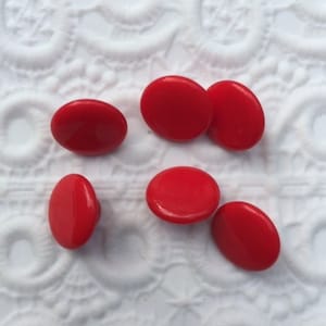 Op de afbeelding: Zes rode plastic knopen, rond en glad, op een witte achtergrond.