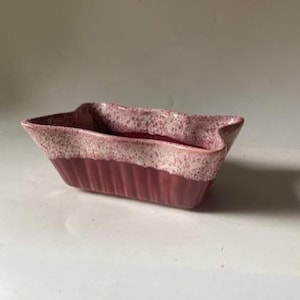 May include: A rectangular ceramic planter with a fluted base and a wavy rim. The lower portion features a solid dark mauve finish, while the upper section and rim are finished in a speckled, lighter pink glaze with a textured, mottled appearance.