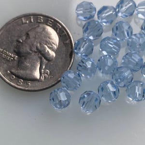 Puede incluir: Primer plano de un mont&oacute;n de cuentas de vidrio azul claro. Las cuentas son facetadas y tienen un acabado brillante. Las cuentas tienen aproximadamente el tama&ntilde;o de una moneda de 25 centavos de d&oacute;lar estadounidense.
