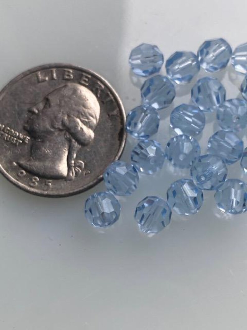 Puede incluir: Primer plano de un mont&oacute;n de cuentas de vidrio azul claro. Las cuentas son facetadas y tienen un acabado brillante. Las cuentas tienen aproximadamente el tama&ntilde;o de una moneda de 25 centavos de d&oacute;lar estadounidense.