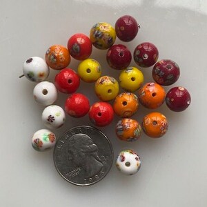 Op de afbeelding: Assortiment van kleurrijke glazen kralen met bloemmotieven. De kralen zijn in tinten rood, geel, oranje en wit.