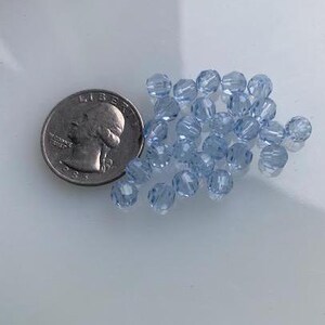 Puede incluir: Un mont&oacute;n de cuentas de vidrio azul claro, aproximadamente del tama&ntilde;o de una moneda de 25 centavos de d&oacute;lar estadounidense.