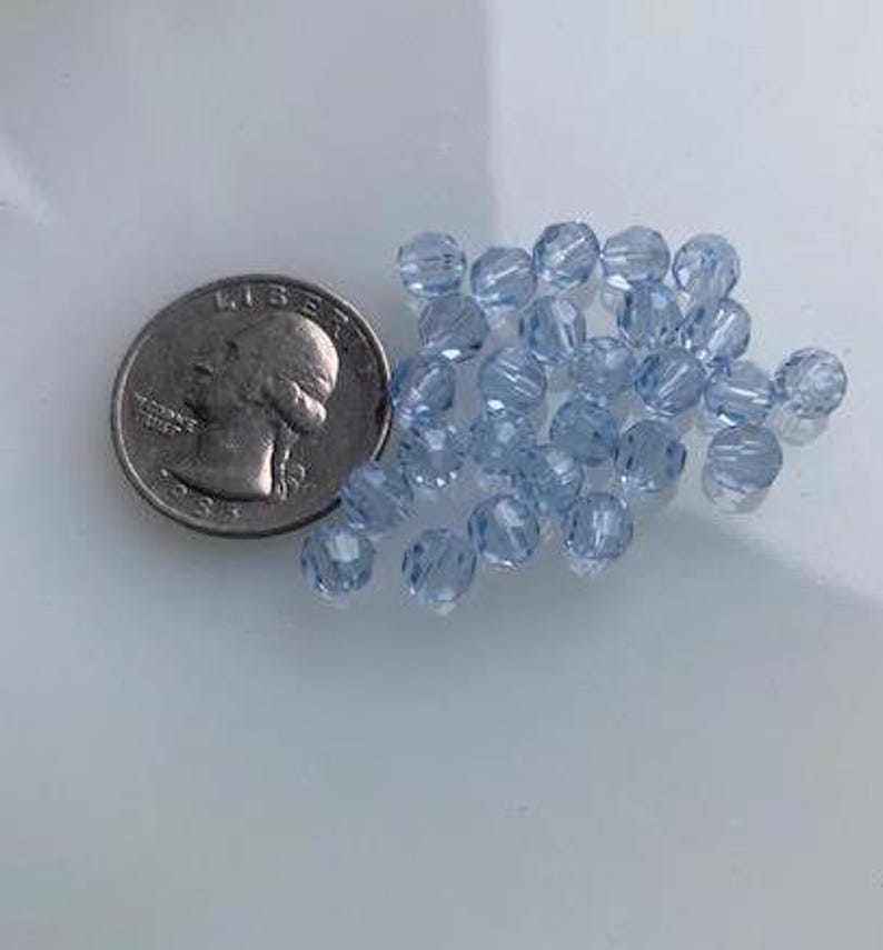 Puede incluir: Un mont&oacute;n de cuentas de vidrio azul claro, aproximadamente del tama&ntilde;o de una moneda de 25 centavos de d&oacute;lar estadounidense.