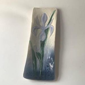 May include: A rectangular ceramic tray with a cream-colored base, featuring a hand-painted light purple iris flower with green leaves. The bottom section of the tray transitions into a deep blue gradient, creating a contrast with the lighter top.
