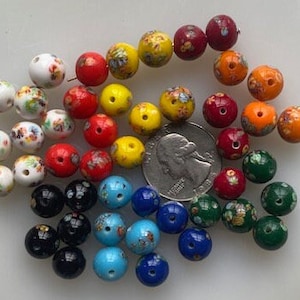Op de afbeelding: Een verzameling kleurrijke glazen kralen met bloemmotieven. De kralen zijn in verschillende tinten rood, geel, blauw, groen en wit. Sommige kralen hebben een gespikkeld of gemarmerd effect.