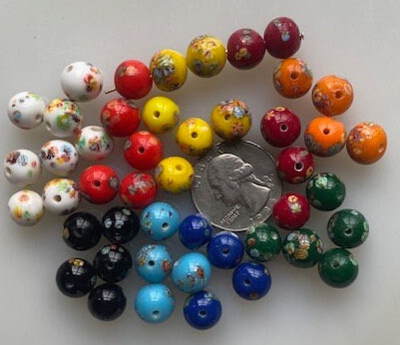 Op de afbeelding: Een verzameling kleurrijke glazen kralen met bloemmotieven. De kralen zijn in verschillende tinten rood, geel, blauw, groen en wit. Sommige kralen hebben een gespikkeld of gemarmerd effect.