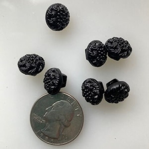 May include: Six black plastic buttons with a raised, textured design. The buttons are round and have a flat back.