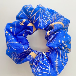 May include: Blue fabric scrunchie with a gold celestial print featuring stars, moons, and sunbursts.