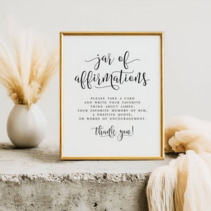 Może przedstawiać: Złoty znak z napisem "jar of affirmations" w czarnym, ozdobnym piśmie. Znak zachęca gości do napisania kartki z ich ulubioną rzeczą o Jamesie, ulubionym wspomnieniem, pozytywnym cytatem lub słowami otuchy.