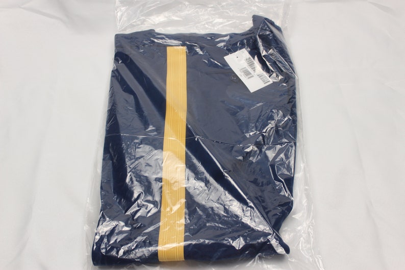 Puede incluir: Una camisa azul marino con una franja dorada en la parte delantera. La camisa est&aacute; doblada y empaquetada en una bolsa de pl&aacute;stico transparente.
