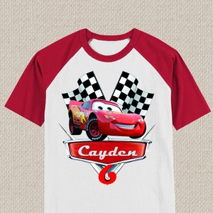 Może przedstawiać: Czerwono-biała koszulka typu raglan z nadrukiem kresk&oacute;wkowego wizerunku Złomka McQueen z filmu Auta, szachownicy i imieniem "Cayden" na przodzie.