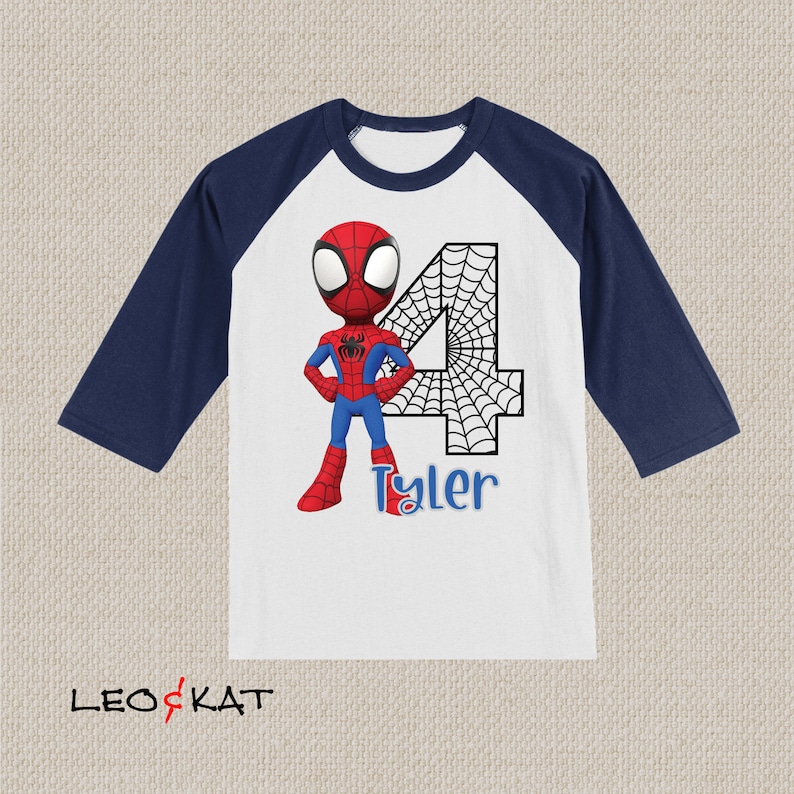 May include: A white and navy blue baseball t-shirt with a cartoon image of Spiderman standing in front of a large number 4 with a spiderweb design. The name Tyler is written below the number.