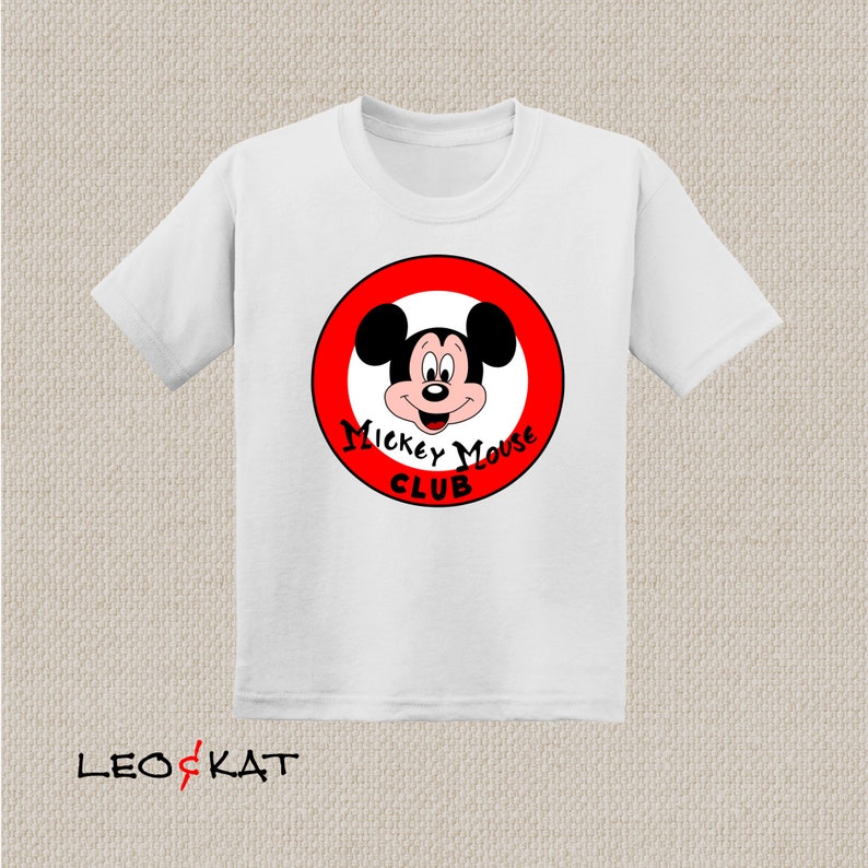 以下が含まれることがあります： 赤い円の中にミッキーマウスの顔が描かれた白いTシャツ。円には「Mickey Mouse Club」という文字が書かれています。