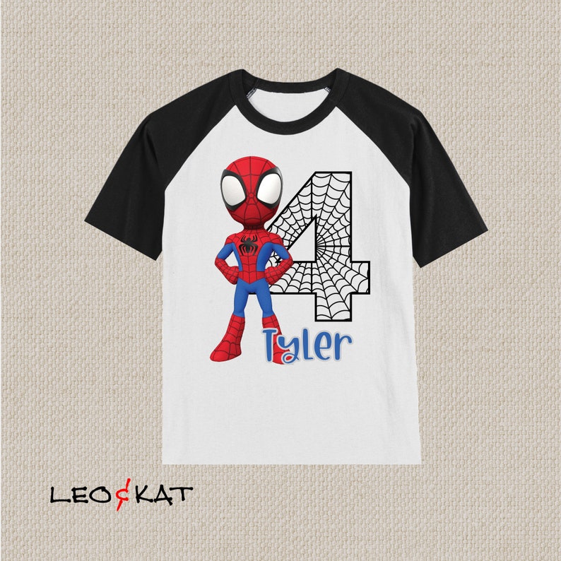 May include: White and black raglan t-shirt with a cartoon image of Spiderman in a red and blue suit standing in front of a black and white number 4 with a spider web design. The text "Tyler" is printed below the number.