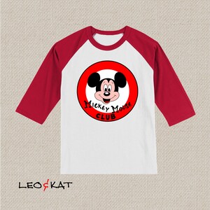 以下が含まれることがあります： 白と赤のベースボールTシャツ。赤い円の中にミッキーマウスの顔が描かれています。円には「Mickey Mouse Club」という文字が書かれています。