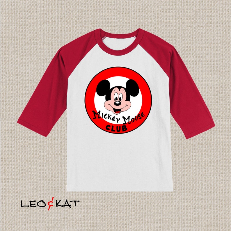 以下が含まれることがあります： 白と赤のベースボールTシャツ。赤い円の中にミッキーマウスの顔が描かれています。円には「Mickey Mouse Club」という文字が書かれています。