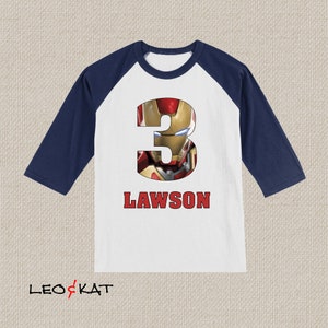 Pu&ograve; includere: Maglietta da baseball bianca e blu navy con un numero tre rosso con un'immagine di Iron Man. La maglietta ha il nome Lawson stampato sotto il numero.