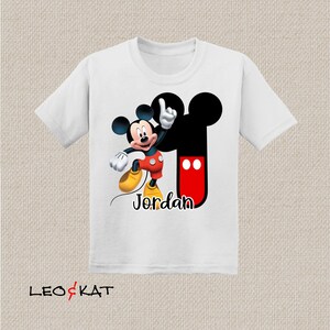 Peut inclure: T-shirt blanc avec un motif Mickey Mouse noir et rouge. Le motif comprend les oreilles embl&eacute;matiques de Mickey Mouse et le texte "Jordan".