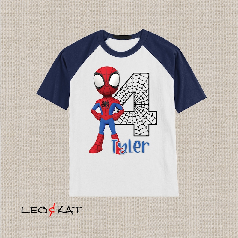 May include: A white and navy blue raglan t-shirt with a cartoon image of Spiderman in a red and blue suit. The number 4 is behind Spiderman with a black spiderweb design. The name Tyler is written below Spiderman.