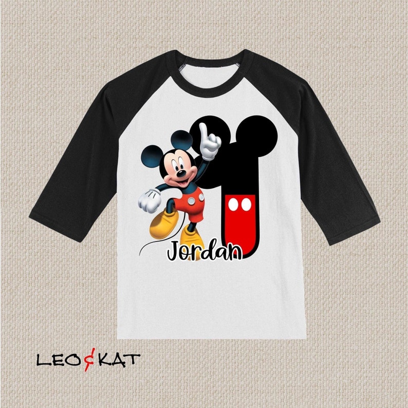 Peut inclure: T-shirt de baseball blanc et noir avec un motif Mickey Mouse rouge et noir. Le t-shirt porte le nom "Jordan" imprim&eacute; sur le devant.