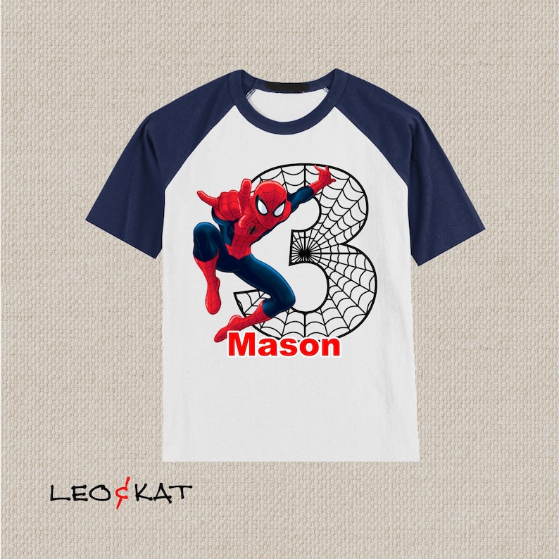Puede incluir: Camiseta de manga raglan blanca y azul marino con un gr&aacute;fico de Spiderman rojo y azul y un dise&ntilde;o de telara&ntilde;a negra alrededor del n&uacute;mero 3. El nombre "Mason" est&aacute; impreso en rojo debajo del gr&aacute;fico.