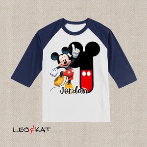 Peut inclure: T-shirt de baseball blanc et bleu marine avec un motif de Mickey Mouse et le nom "Jordan" imprim&eacute; sur le devant.