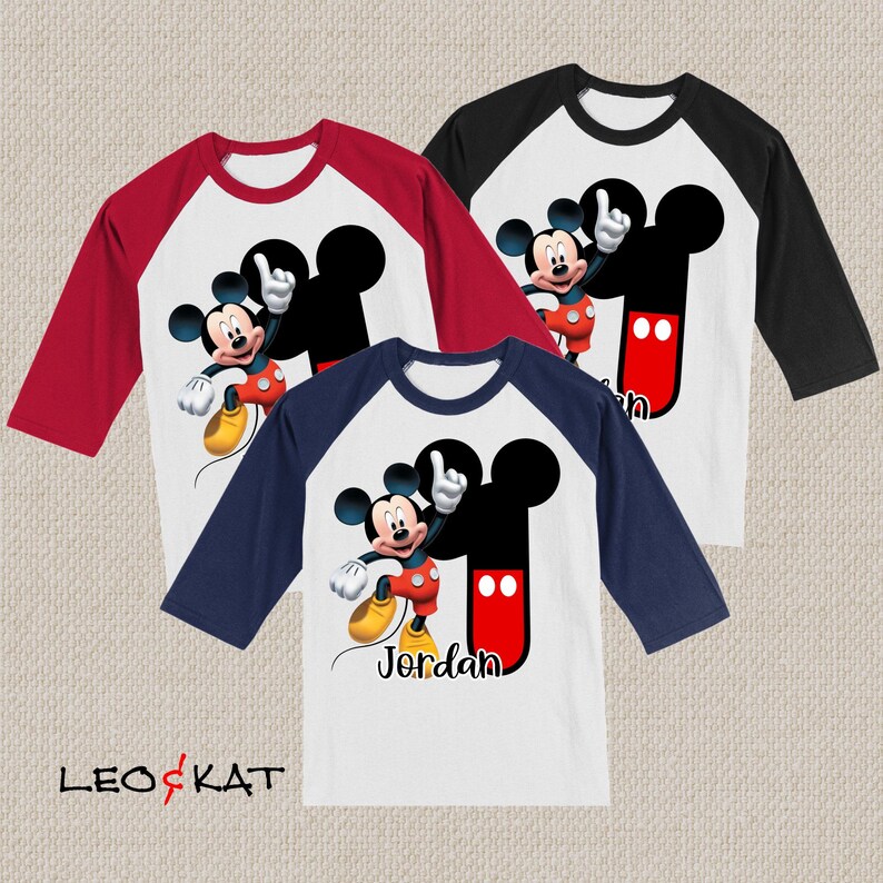 Peut inclure: Trois t-shirts de style baseball avec une manche rouge, bleu marine et noire. Chaque t-shirt pr&eacute;sente un devant blanc avec un motif Mickey Mouse et le nom "Jordan" imprim&eacute; en bas.