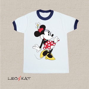 K&ouml;nnte beinhalten: Wei&szlig;es T-Shirt mit blauem Ringelkragen und einem Motiv von Minnie Maus, die einen roten Rock mit wei&szlig;en Punkten und eine rote Schleife tr&auml;gt.