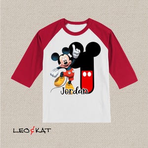 Peut inclure: T-shirt de style baseball rouge et blanc avec un motif Mickey Mouse rouge et noir et le nom "Jordan" imprim&eacute; sur le devant.