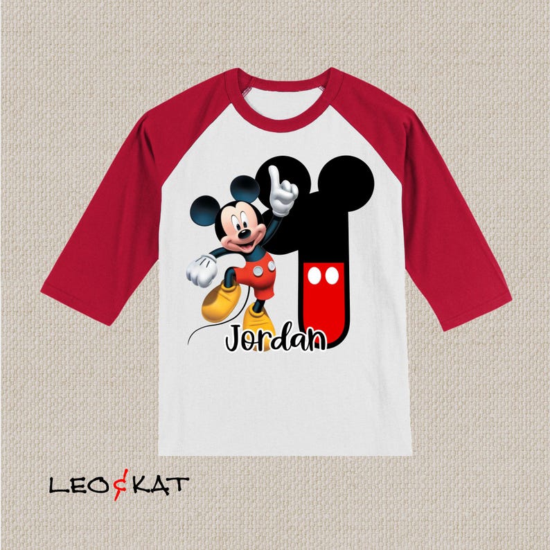 Peut inclure: T-shirt de style baseball rouge et blanc avec un motif Mickey Mouse rouge et noir et le nom "Jordan" imprim&eacute; sur le devant.