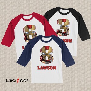 Pu&ograve; includere: Tre maglie da baseball con maniche rosse, nere e blu navy. Le maglie presentano un davanti bianco con un numero e il nome "Lawson" stampato sul davanti. I numeri sono 3, 6 e 8 e ogni numero &egrave; composto da un'immagine del viso di Iron Man.