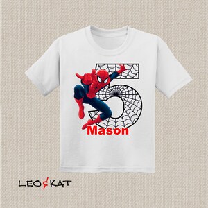 Puede incluir: Camiseta blanca con un gr&aacute;fico de Spiderman rojo y azul, un dise&ntilde;o de telara&ntilde;a negra y el n&uacute;mero 5. El nombre Mason est&aacute; escrito debajo del gr&aacute;fico.