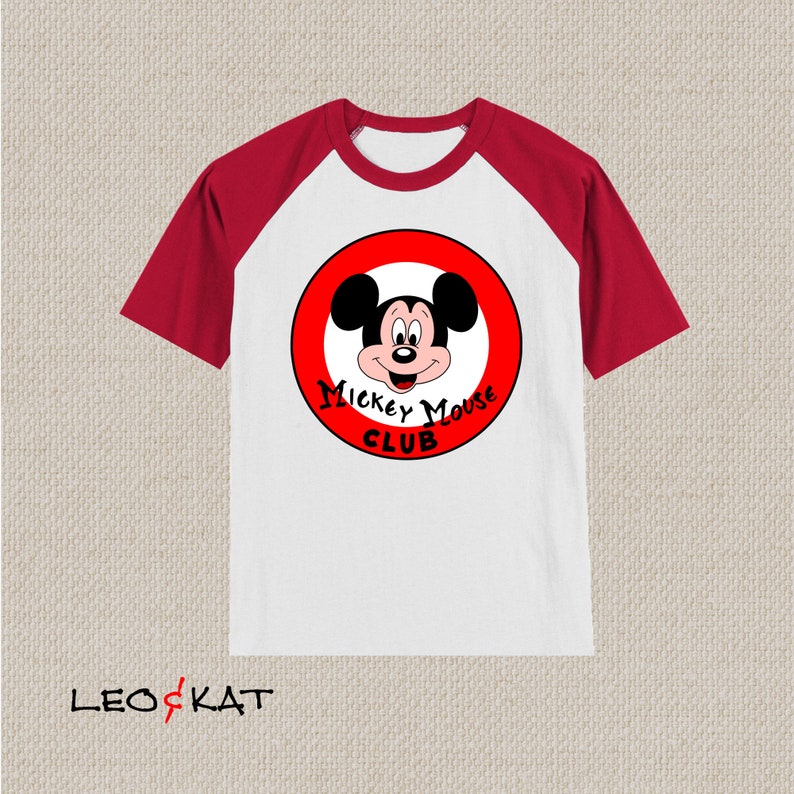 以下が含まれることがあります： 白と赤のラグランスリーブTシャツ。赤い円の中にミッキーマウスと「Mickey Mouse Club」の文字が描かれています。