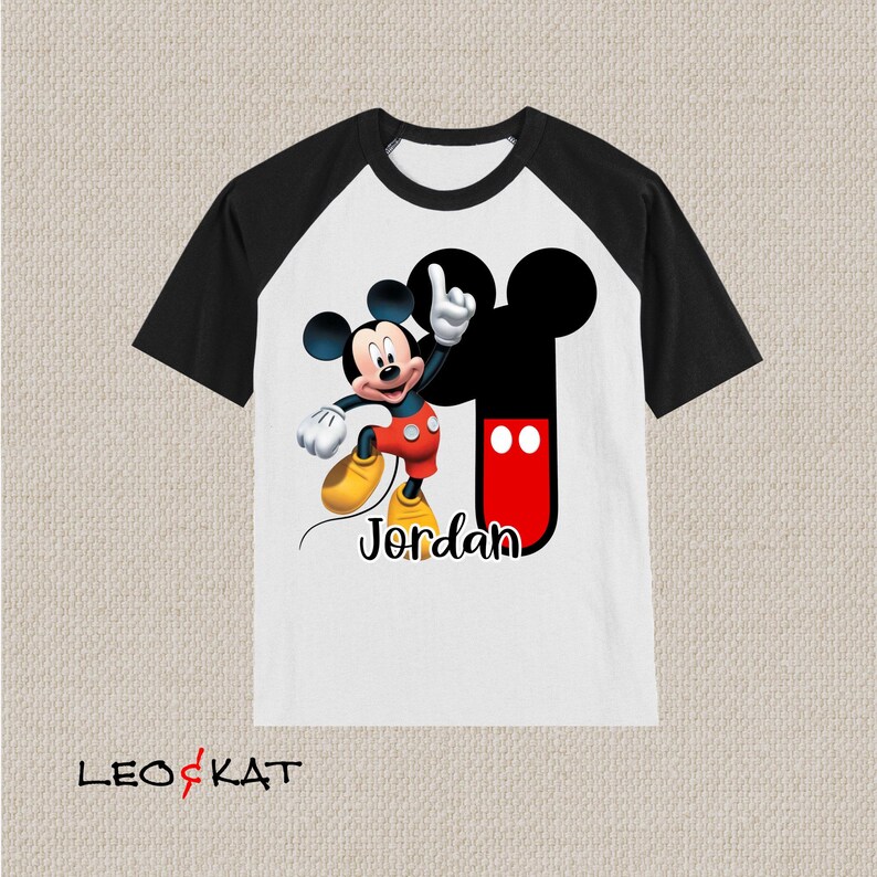 Peut inclure: T-shirt &agrave; manches raglan blanche et noire avec un motif Mickey Mouse et le nom "Jordan" imprim&eacute; sur le devant.