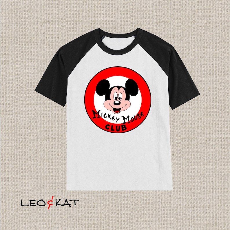 以下が含まれることがあります： 白と黒のラグランスリーブTシャツ。赤い円形のグラフィックにはミッキーマウスと「ミッキーマウスクラブ」の文字が描かれています。